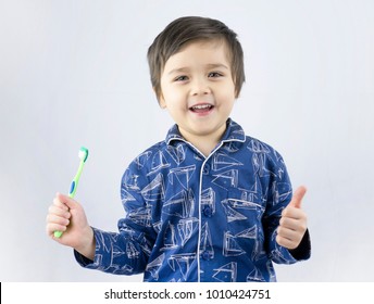 Cheerful Little Boy Wearing Pajamas Holding A Tooth Brush And Showing Thumbs Up Over White Background, Studio Portrait Of A Healthy Mixed Race Boy With A Toothbrush Isolated.