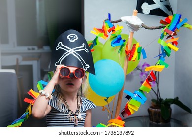 A cheerful little child in a pirate costume plays at home on a cardboard sea ship with a black flag. Fun games at home with family. Travels and adventures at home
