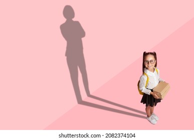 Cheerful Little Child In School Uniform And Glasses With Backpack Holds Books And Shadow Of Businesswoman On The Wall, Pink Background, Conceptual Image For Kids Big Dreams, Copy Space