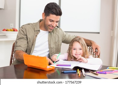 Cheerful little girl colouring at the table and her father at home in kitchen