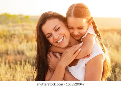 Cheerful little girl embracing smiling woman from back while spending time in field on sunny day together - Powered by Shutterstock