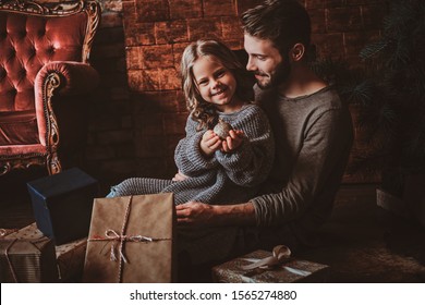 Cheerful little girl is holding christmas decoration ball while sitting with her father on the floor, surrounded with gifts.