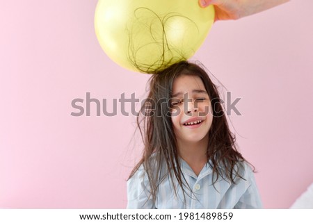 The cheerful little girl in pajama with electrified hair during the electrification balloon experiment for school on pink background.
