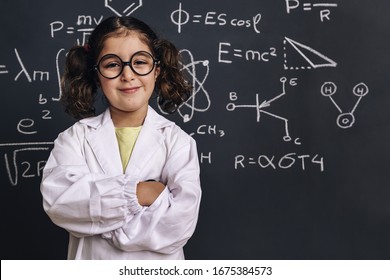 cheerful little girl science student with glasses in lab coat smiles on school blackboard background with hand drawings science formula pattern, back to school and successful female career concept - Shutterstock ID 1675384573