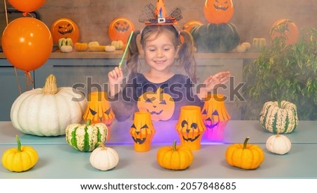 Cheerful little girl shows magic tricks with a magic wand for Halloween. Multi-colored smoke over the table of the sorceress. The little witch has bewitched the pumpkins. Fun games for Halloween.