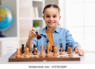 Cheerful little girl  smiling and looking at camera while making movie with black queen during match in light classroom in daytime - Powered by Shutterstock