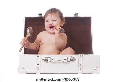 Cheerful little girl with two make-up brushes sitting in a suitcase on isolated white
