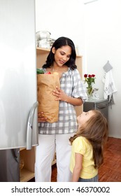 Cheerful Little Girl Unpacking Grocery Bag With Her Mother In The Kitchen