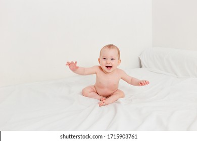 Cheerful Little Girl Without Clothes Sits On The Bed On A White Background