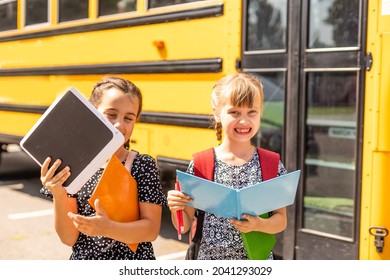 Cheerful little girls next to school bus. Backback. Back to school concept.
