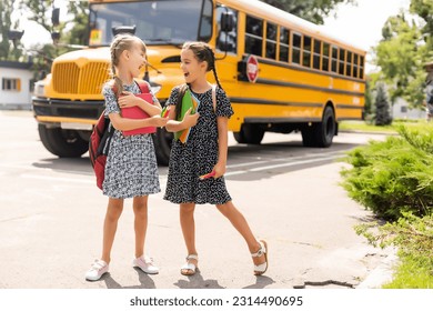 Cheerful little girls next to school bus. Backback. Back to school concept.