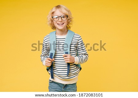 Cheerful little male kid teen boy 10s years old wearing casual striped sweatshirt eyeglasses backpack looking camera isolated on yellow color background, child studio portrait. Education concept