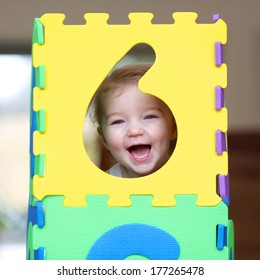 Cheerful little toddler girl playing hide and seek with colorful numbers puzzles