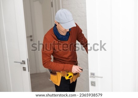 Cheerful locksmith installing a door lock on a new white door