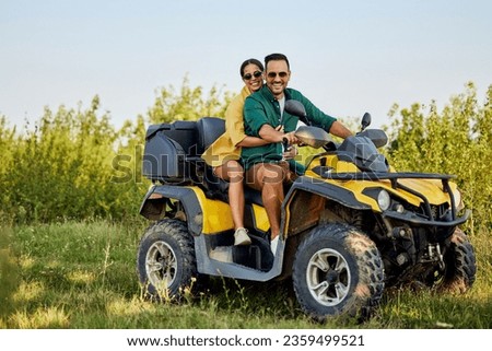 A cheerful love couple having an adventure on a quad bike, driving through beautiful nature, smiling for the camera.