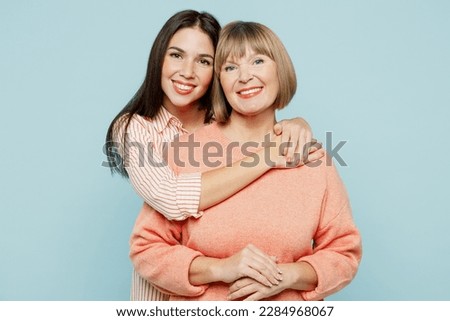 Cheerful lovely fun satisfied elder parent mom with young adult daughter two women together wearing casual clothes hugging cuddle look camera isolated on plain blue cyan background. Family day concept