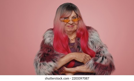 Cheerful Lovely Stylish Elderly Woman In Coat Smiling, Looking At Camera. Senior Fashion Model Grandmother With Pink Hairstyle Coiffure Indoor Studio Isolated On Pink Background. Female Nature Beauty