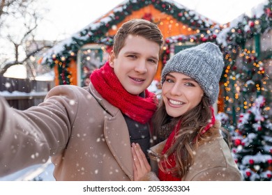 Cheerful lovers young man and woman taking selfie while spending snowy winter day together outside, loving millennial couple celebrating winter holidays, taking photo at backyard while snowing - Powered by Shutterstock