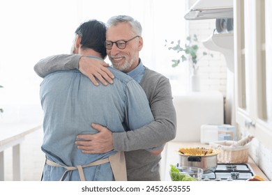 Cheerful loving caring old elderly senior father embracing hugging his adult caucasian son in the kitchen while cooking lunch, dinner, preparing meal together. Happy father`s day! I love you, dad! - Powered by Shutterstock