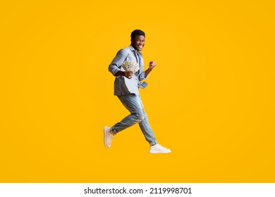 Cheerful Lucky Handsome Young African American Man Got Loan Or Won Lottery, Showing Cash, Clenching Fist And Jumping Up Over Yellow Studio Background, Copy Space, Full Length Shot