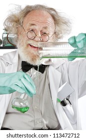 Cheerful Mad Senior Scientist In Lab Measures Green Liquid In Beaker. Closeup, Frizzy Grey Hair, Round Glasses, Lab Coat, Aqua Rubber Gloves, Vertical, High Key.