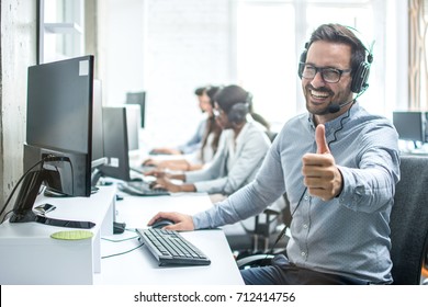 Cheerful male customer service operator showing thumbs up in office.