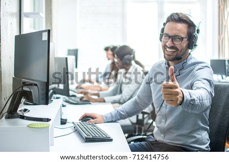 Cheerful male customer service operator showing thumbs up in office.