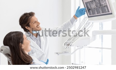 Cheerful male dentist doctor showing his patient x-ray results on lcd display, side view, copy space