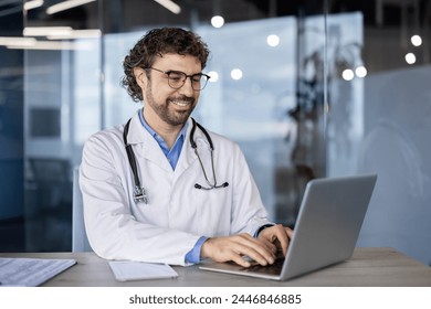 Cheerful male doctor with a stethoscope sitting at a desk, working on a laptop in a bright, contemporary clinic setting. - Powered by Shutterstock