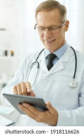 Cheerful Male Doctor Using Tablet Computer In Clinic