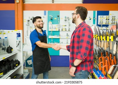 Cheerful male employee smiling shaking hands with a young man and greeting him to the hardware store during his shopping