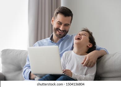 Cheerful male family happy dad and cute kid son bonding laughing watching funny cartoons comedy on laptop at home, smiling father hug small child boy having fun together using computer sit on sofa