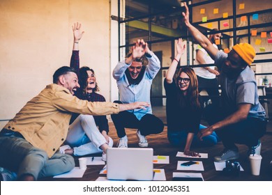 Cheerful male and female students celebrating winning in college contest giving high five, emotional multiracial members of crew excited with success in productive working process on startup