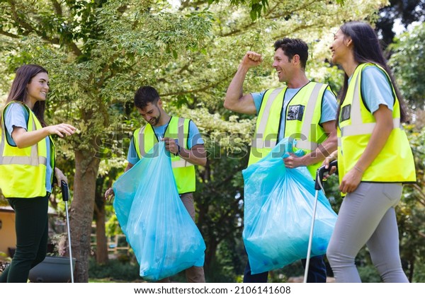 Cheerful male and\
female volunteers collecting garbage in plastic bags during cleanup\
in park. environmental cleanup, social issues, responsibility and\
recycling concept.