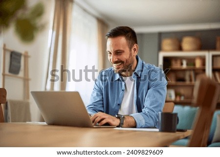 A cheerful male freelancer answering his client via email about a new project, typing on his laptop and sitting at a desk.