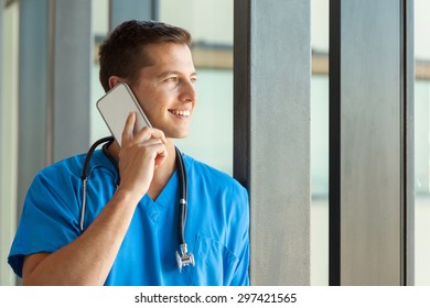 Cheerful Male Nurse Talking On Mobile Phone In Clinic