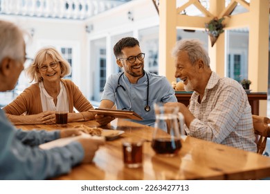 Cheerful male nurse using touchpad while communicating with senior people on patio at residential care home. - Powered by Shutterstock