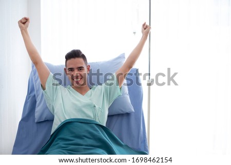 Cheerful male patient with happy hands gesture resting in hospital room. Smiling  recovering patient pay medical fee by healthcare insurance. Happy patient with hands thumbs up gesture concept. 