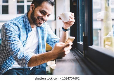 Cheerful male person happy to receive messages from friend checking mail via smartphone during rest in cafe, smiling man satisfied with getting good news using telephone fr networking drinking coffee - Powered by Shutterstock