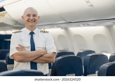 Cheerful male pilot in uniform keeping arms crossed and smiling at camera while standing inside of the airplane. Transportation, aircrew concept - Shutterstock ID 2026324520