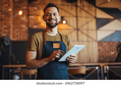 A cheerful male waiter in an apron holds a digital tablet, ready to take orders in a modern bar, exuding cheerful professionalism in his service role. - Powered by Shutterstock