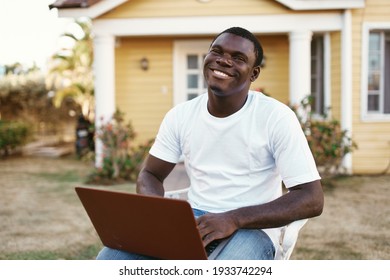 Cheerful man of african appearance outdoors with laptop