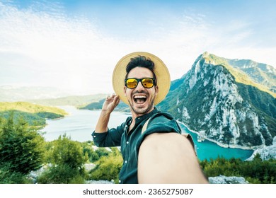 Cheerful man with backpack taking selfie picture on mountain landscape - Smiling hiker having fun on excursion day - Delightful tourist enjoying autumn vacation into the wild - Traveling life style - Powered by Shutterstock