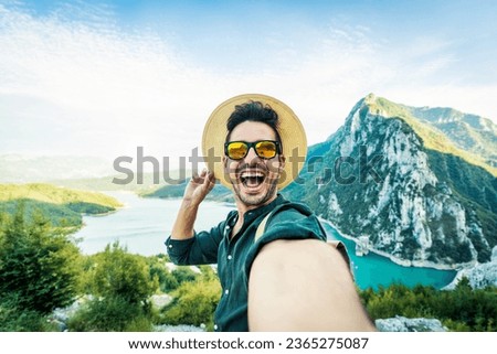 Cheerful man with backpack taking selfie picture on mountain landscape - Smiling hiker having fun on excursion day - Delightful tourist enjoying autumn vacation into the wild - Traveling life style