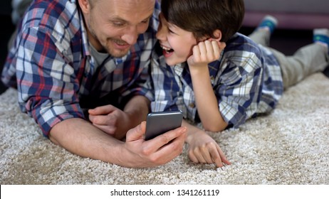 Cheerful man and boy laughing after watching funny video on smartphone, joy