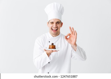 Cheerful Man Chef Cook Wearing Uniform Showing Pastry On A Plate Isolated Over White Background