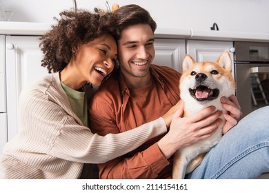 cheerful man cuddling shiba inu dog near smiling african american girlfriend in kitchen - Powered by Shutterstock