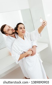 Cheerful Man With Duck Face Taking Selfie While Hugging Girlfriend In Bathroom 