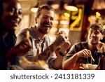 Cheerful man eating hamburger while gathering with friends in a bar. 