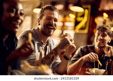 Cheerful man eating hamburger while gathering with friends in a bar.  - Powered by Shutterstock